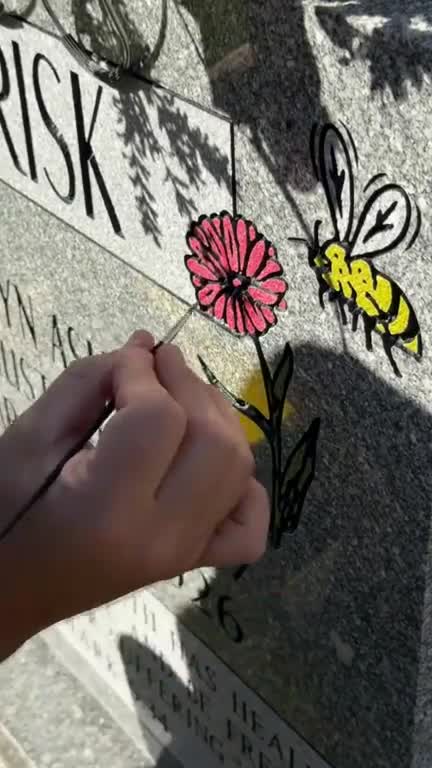 Mark Loboda of Reserve Memorials hand-painting a pink flower and a yellow bee onto the RISK family headstone